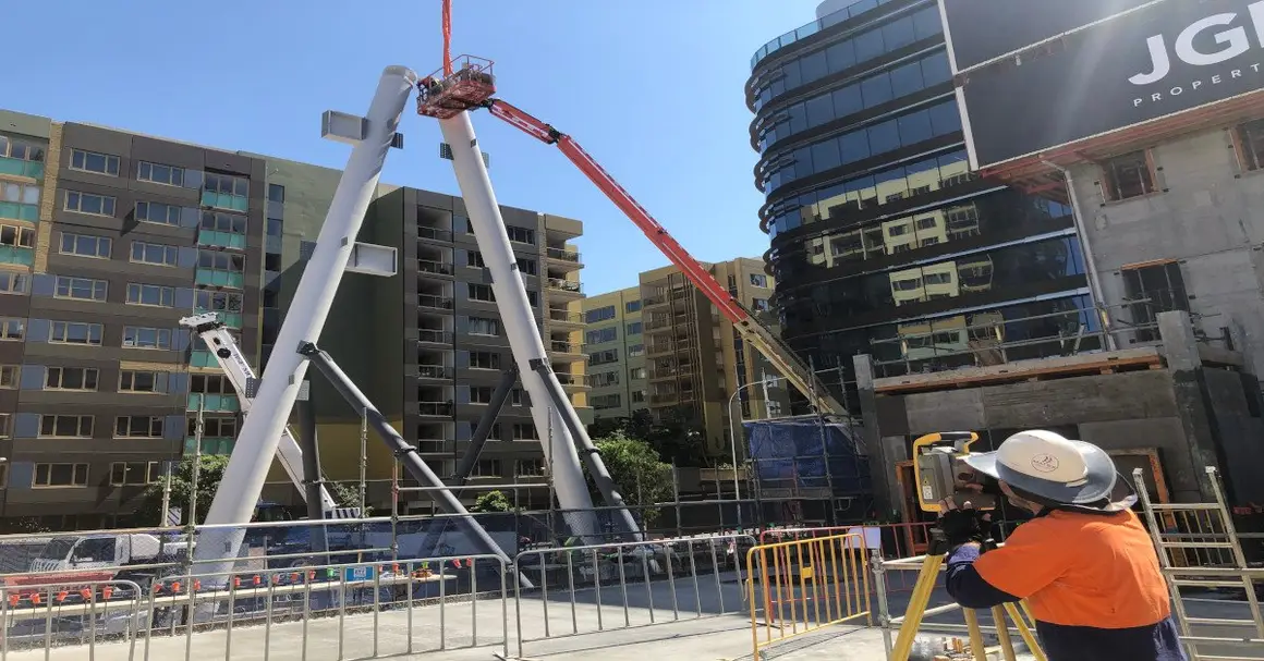 Land Solution surveyor with a total station checking the position of exoskeleton steel members as they are lifted into place