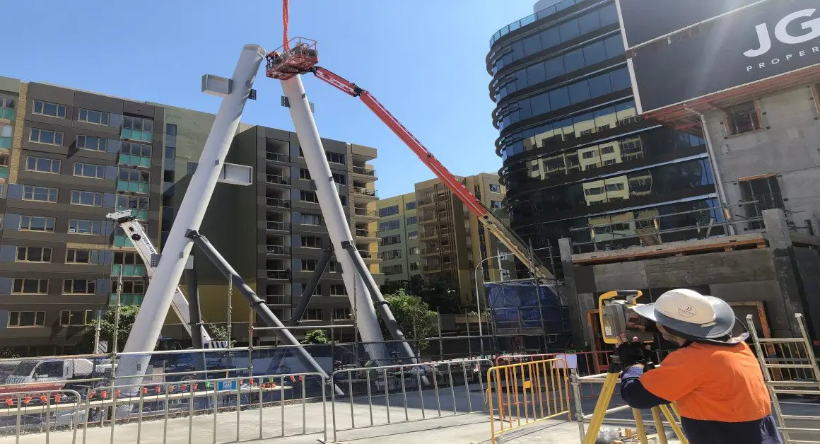 Land Solution surveyor with a total station checking the position of exoskeleton steel members as they are lifted into place