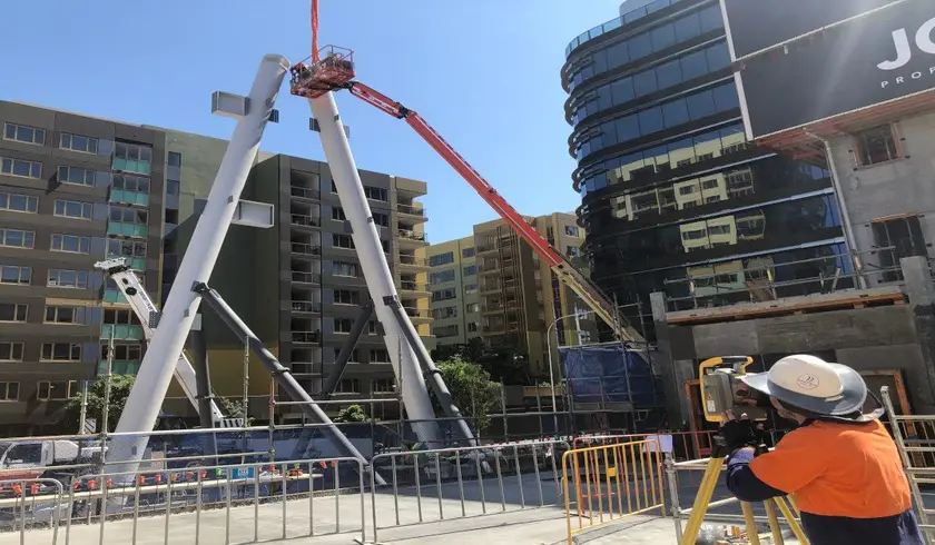 Land Solution surveyor with a total station checking the position of exoskeleton steel members as they are lifted into place