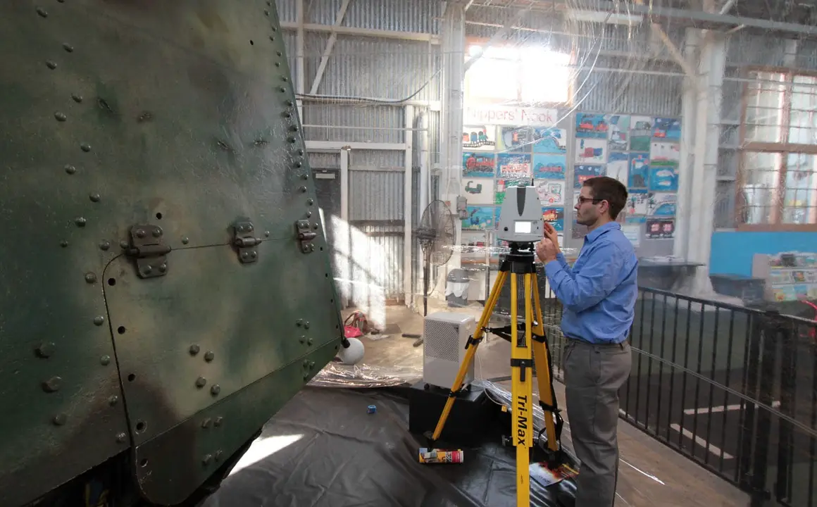 Surveyor operating a laser scanner beside the riveted hull of Mephisto