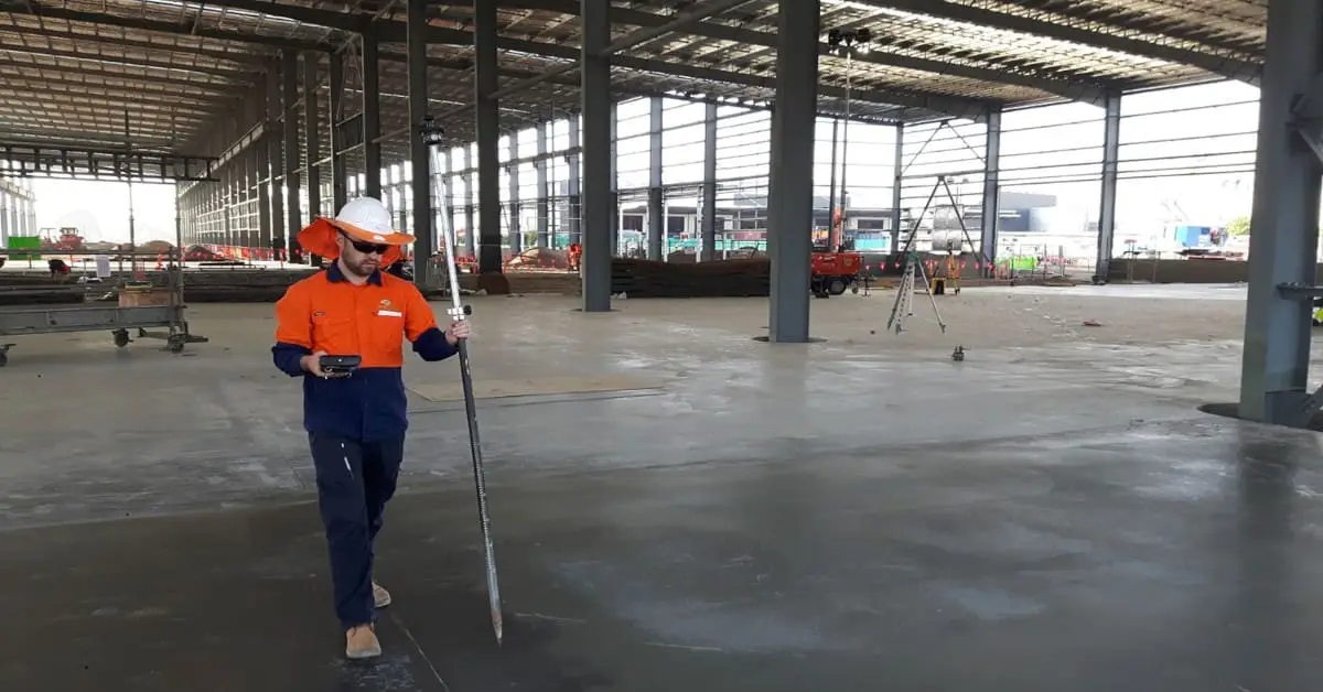 Surveyor setting out on the concrete slab inside the steel-framed MILVEHCOE building at Redbank