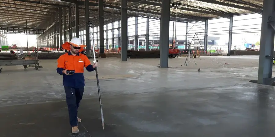 Surveyor setting out on the concrete slab inside the steel-framed MILVEHCOE building at Redbank