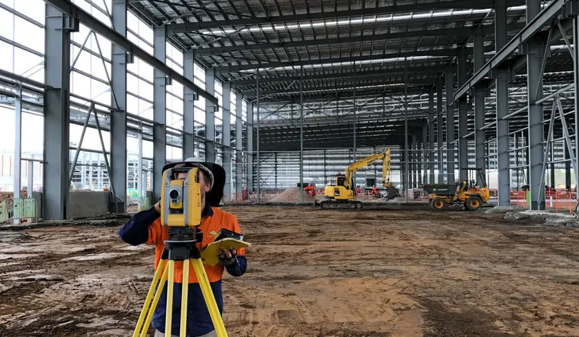 Surveyor with a total station inside the MILVEHCOE warehouse during construction